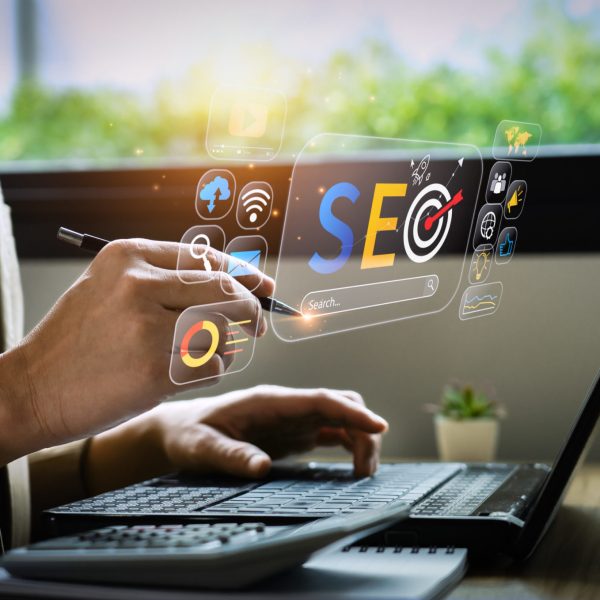 une main tenant un stylo devant un ordinateur portable dans un environnement lumineux