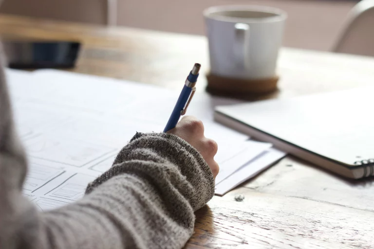 personne écrivant sur une feuille de papier avec tasse en train de se former